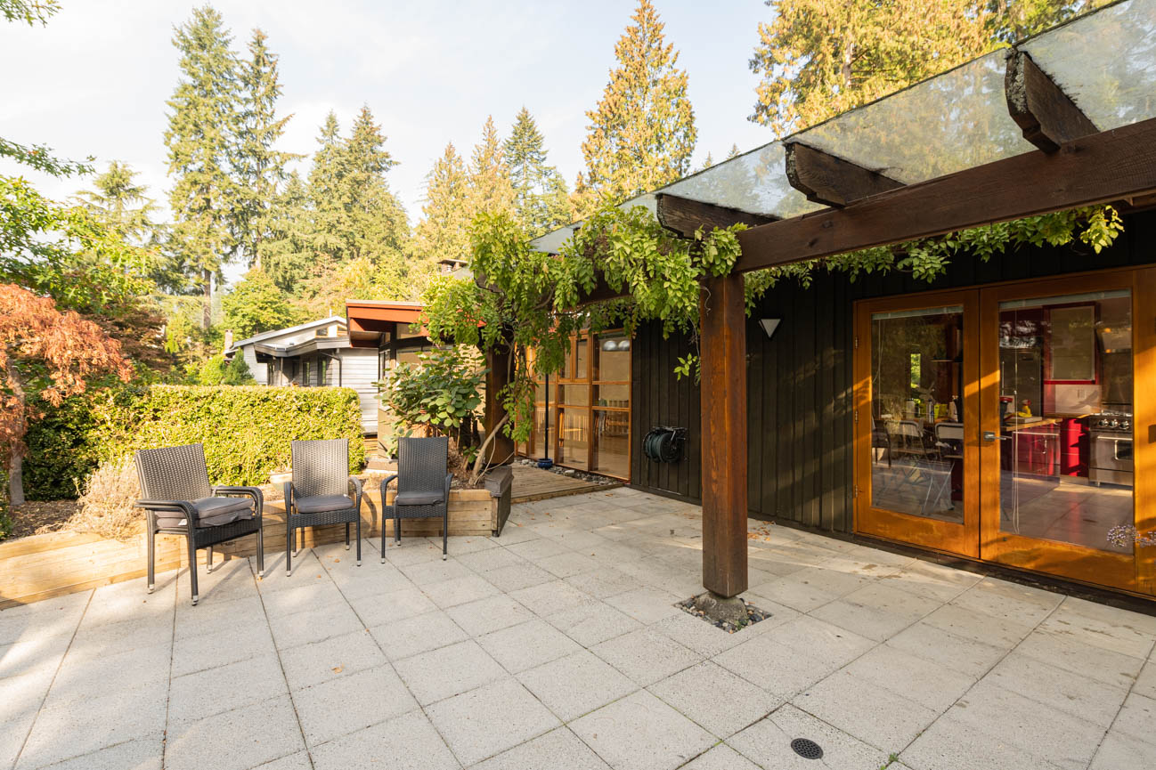 Furnished patio with outdoor seating and greenery, leading to a modern kitchen with glass doors. - Upper - 3248 Robinson Road, North Vancouver