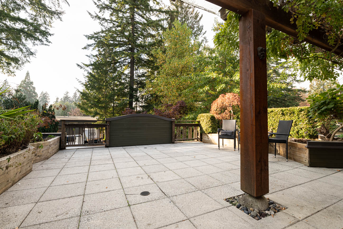 Furnished patio with stone flooring and wooden pergola, surrounded by lush greenery. - Upper - 3248 Robinson Road, North Vancouver