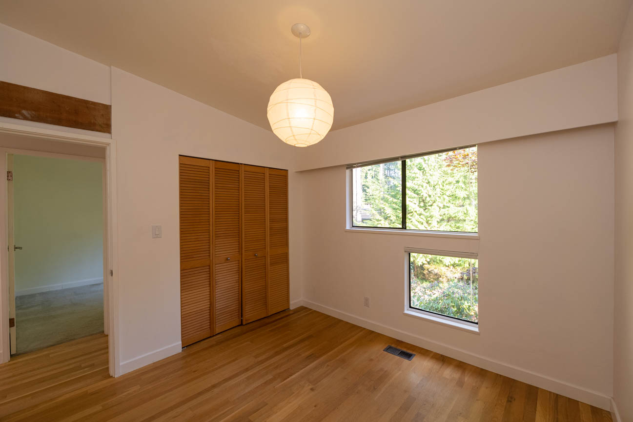 Bright bedroom with wooden closet doors and hardwood floors, natural light from windows. - Upper - 3248 Robinson Road, North Vancouver