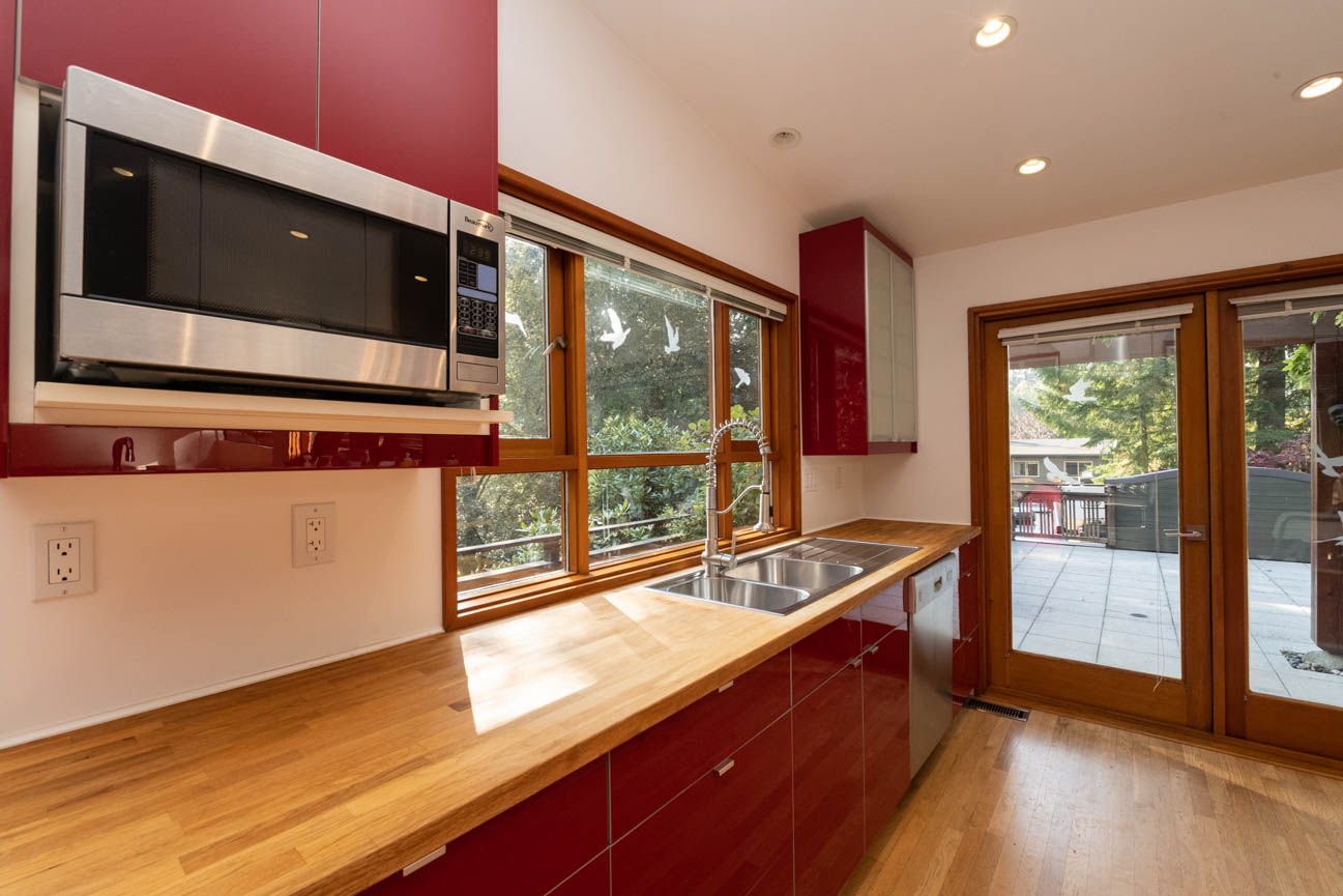 Bright kitchen with red cabinets, hardwood floors, and a view of trees outside. - Upper - 3248 Robinson Road, North Vancouver