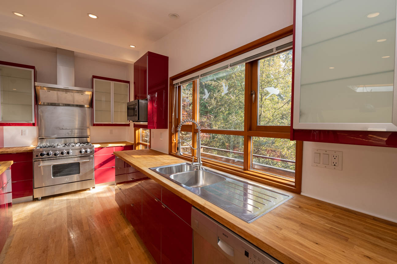 Bright kitchen with red cabinets, hardwood floors, and large windows overlooking trees. - Upper - 3248 Robinson Road, North Vancouver