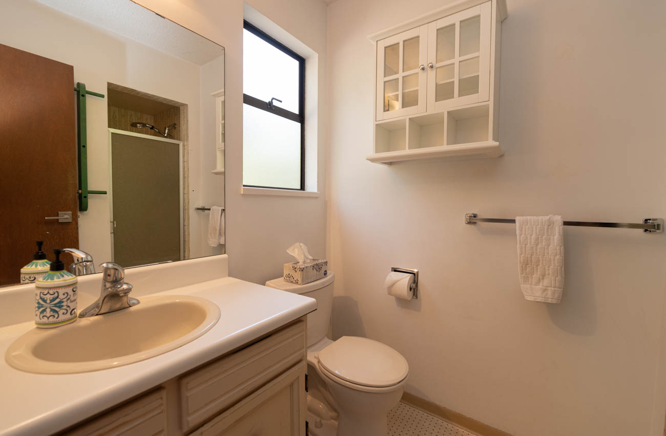 Bright bathroom with white countertop and sink, small window, and wooden door. - Upper - 3248 Robinson Road, North Vancouver