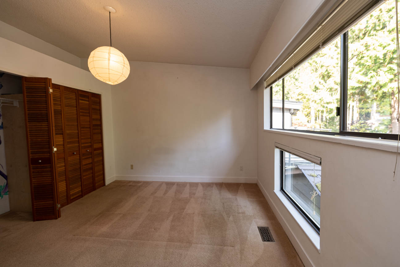 Bright bedroom with wooden closet doors and large windows, letting in natural light. - Upper - 3248 Robinson Road, North Vancouver