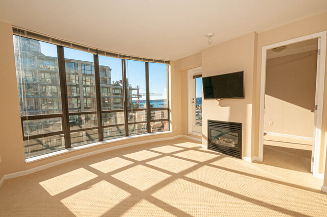 Bright living room with floor-to-ceiling windows offering a city view, plus a fireplace and wall-mounted TV.