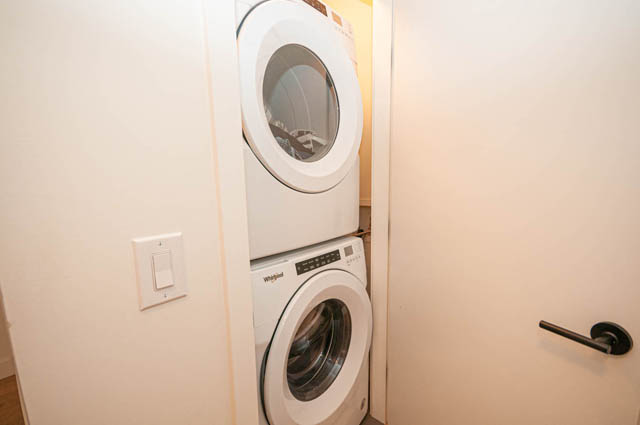Bright laundry room with stacked washer and dryer, white walls, and a light switch. - 30 - 533 East 3rd st., North Vancouver