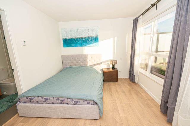 Bright bedroom with hardwood floors and a large window, showcasing a serene view. - 30 - 533 East 3rd st., North Vancouver