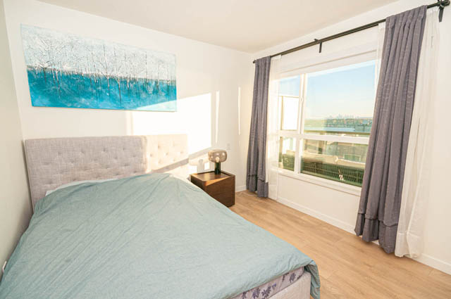 Bright bedroom with light blue bedding, hardwood floors, and a city view. - 30 - 533 East 3rd st., North Vancouver