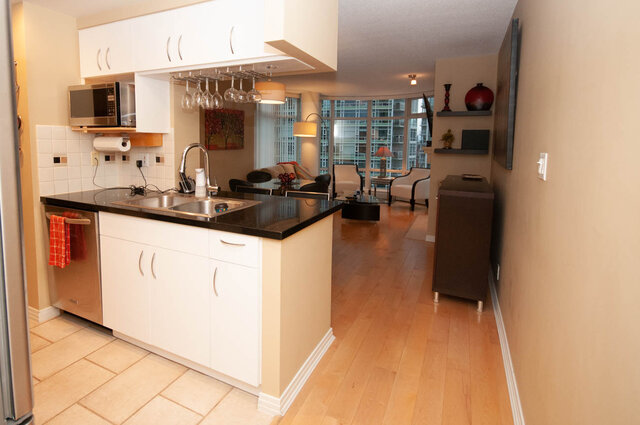 Bright kitchen with black countertops and hardwood floors, featuring a city view from the living area.