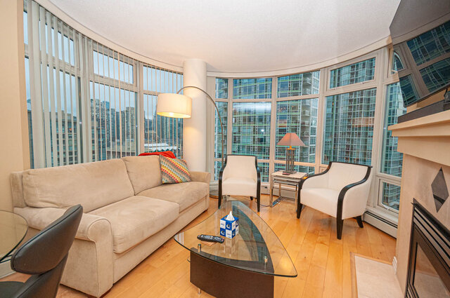 Spacious living room with hardwood floors, large windows offering a city view, and a comfortable sofa set.