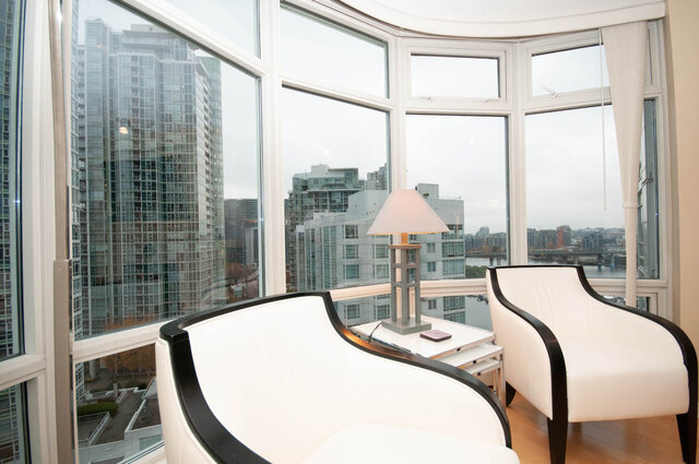 Spacious living room with curved white sofa, large windows offering a stunning city view. - 1605 - 1199 Marinaside Crescent, Vancouver Downtown