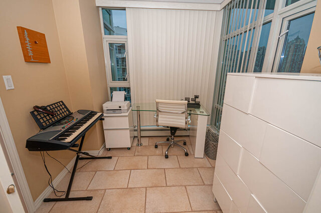 Bright home office with a city view, featuring a glass-top desk and a keyboard setup. - 1605 - 1199 Marinaside Crescent, Vancouver Downtown