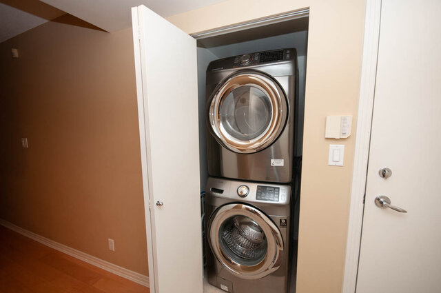 Compact laundry room with stacked washer and dryer, hardwood floors, and neutral walls. - 1605 - 1199 Marinaside Crescent, Vancouver Downtown