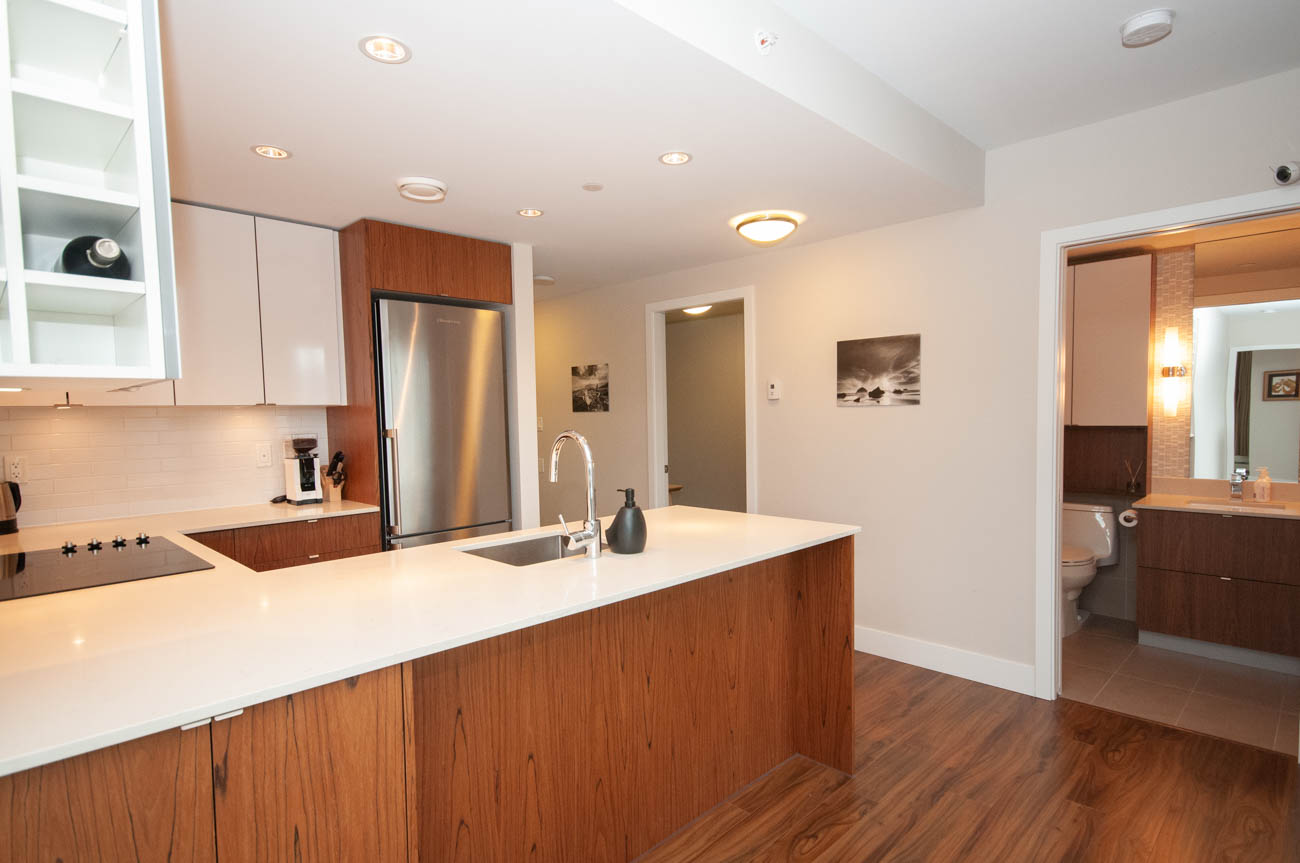 Bright kitchen with white countertops and wooden cabinetry, modern design. - 1403 - 159 West 2nd, Vancouver West Side