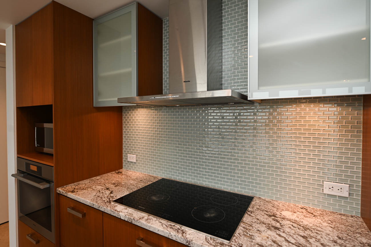 Bright kitchen with granite countertops and modern glass backsplash, featuring a sleek induction cooktop and stainless...