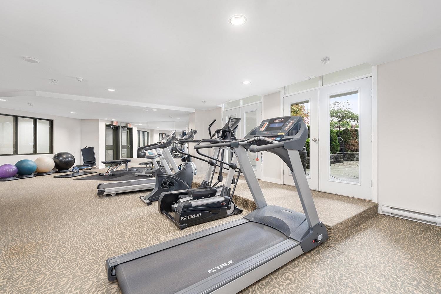 Modern gym with True treadmills and stability balls on patterned carpet. - 807 - 4078 Knight Street, Vancouver East Side