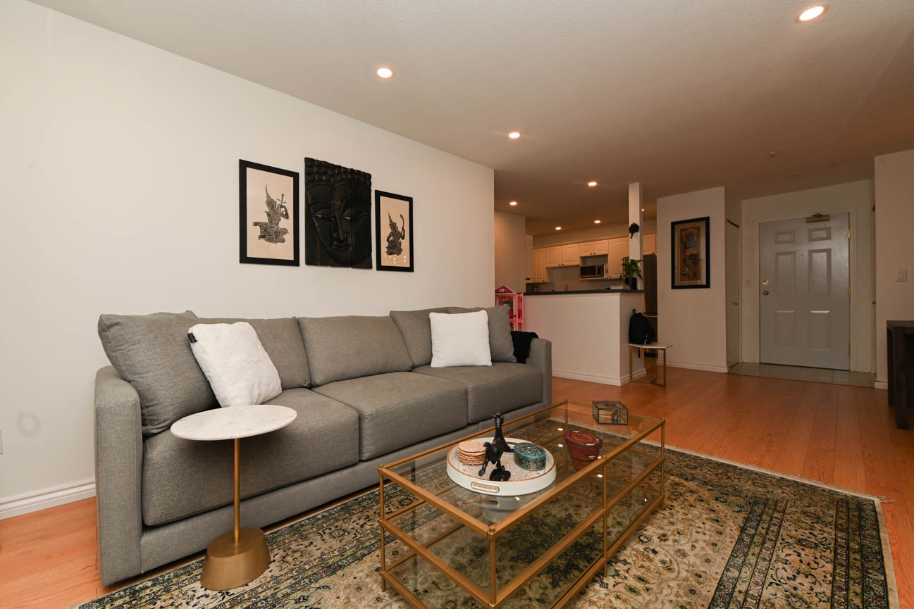 Bright living room with hardwood floors, modern furniture, and a city view. - 208-128 8th Street West, North Vancouver