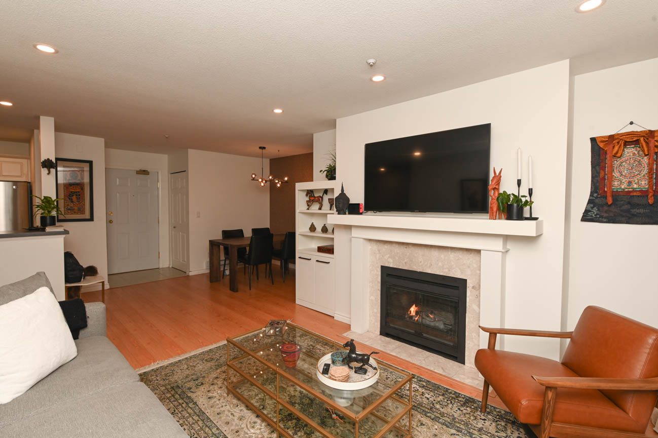 Furnished living room with hardwood floors, modern fireplace, and glass coffee table. - 208-128 8th Street West, North Vancouver