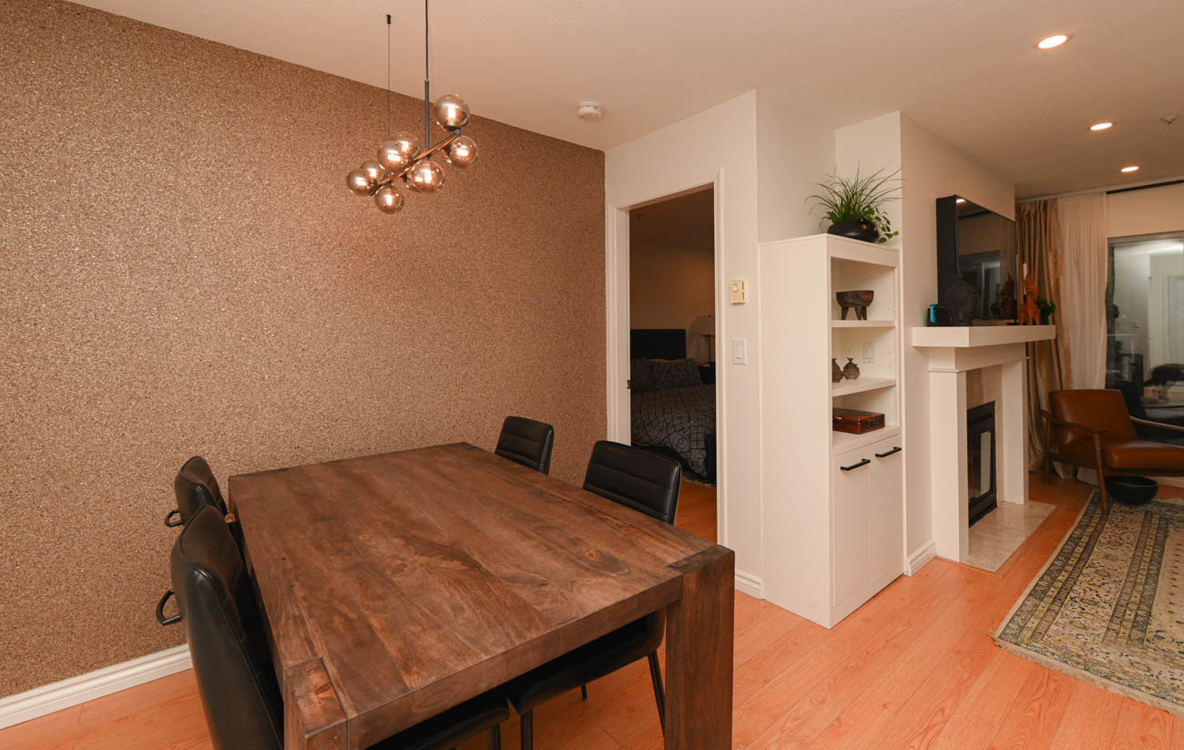 Furnished dining area with cork wall, wooden table, and black chairs. - 208-128 8th Street West, North Vancouver