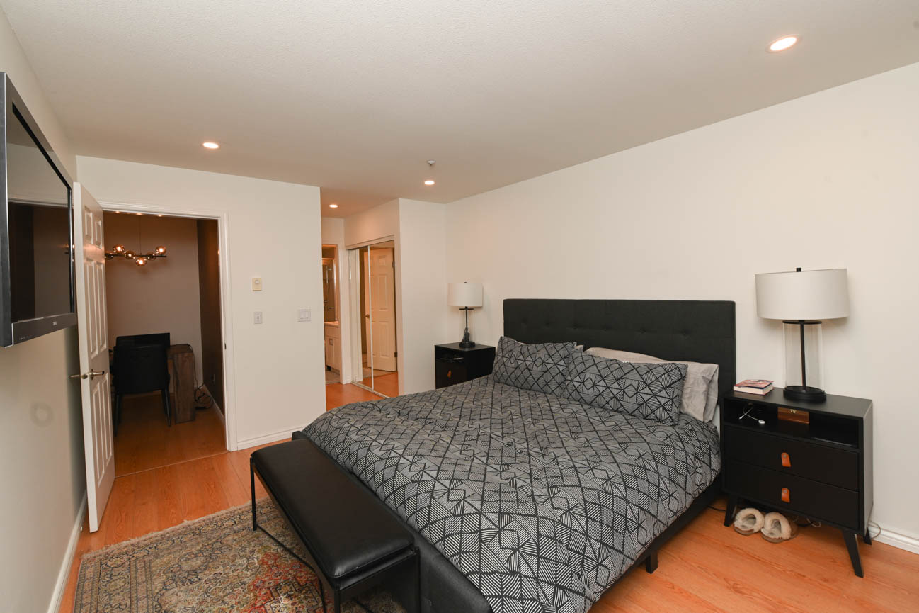 Furnished bedroom with hardwood floors, black headboard, and geometric patterned bedding. - 208-128 8th Street West, North Vancouver