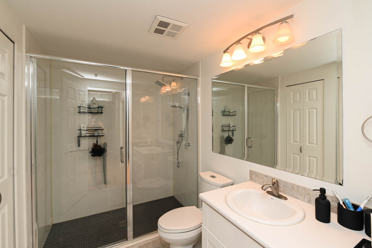 Bright bathroom with white vanity, glass shower, and modern lighting. - 208-128 8th Street West, North Vancouver