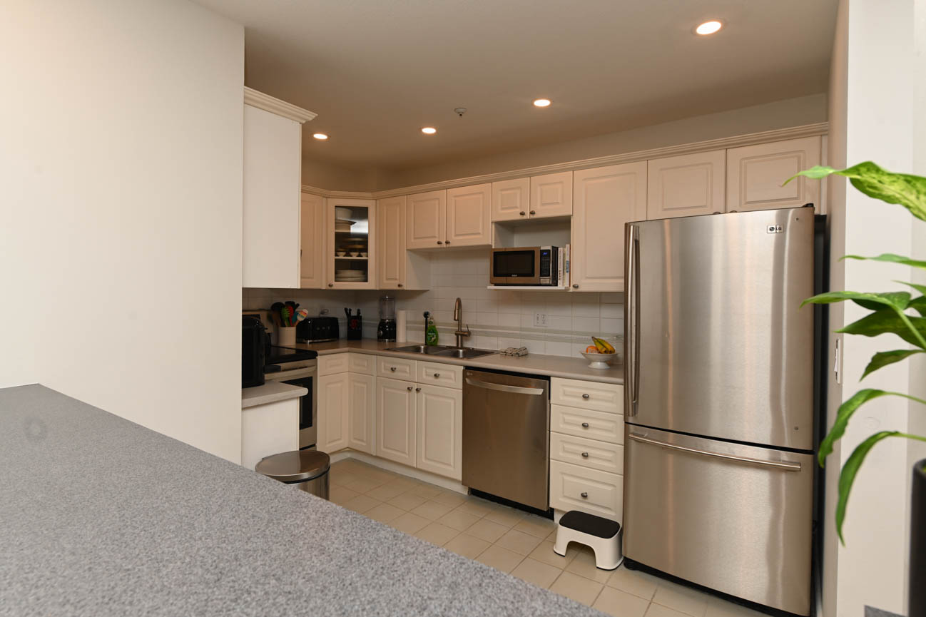 Bright kitchen with white cabinets, stainless steel appliances, and granite countertops. - 208-128 8th Street West, North Vancouver