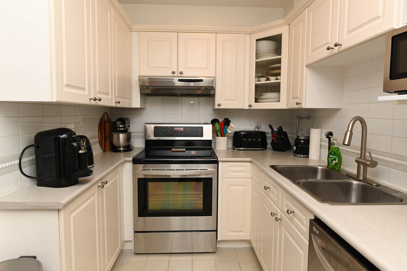 Bright kitchen with white cabinets, stainless steel appliances, and a sink. - 208-128 8th Street West, North Vancouver