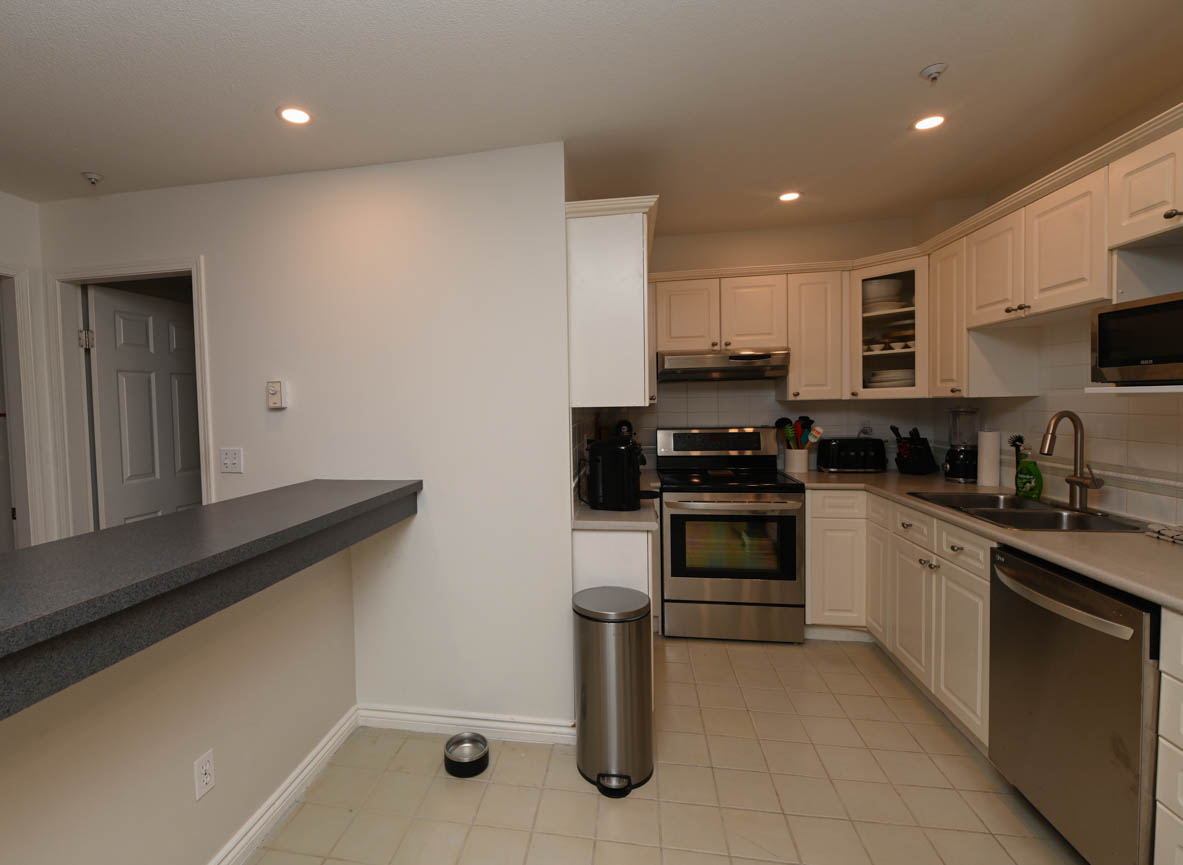Bright kitchen with white cabinets, stainless steel appliances, and a granite countertop. - 208-128 8th Street West, North Vancouver