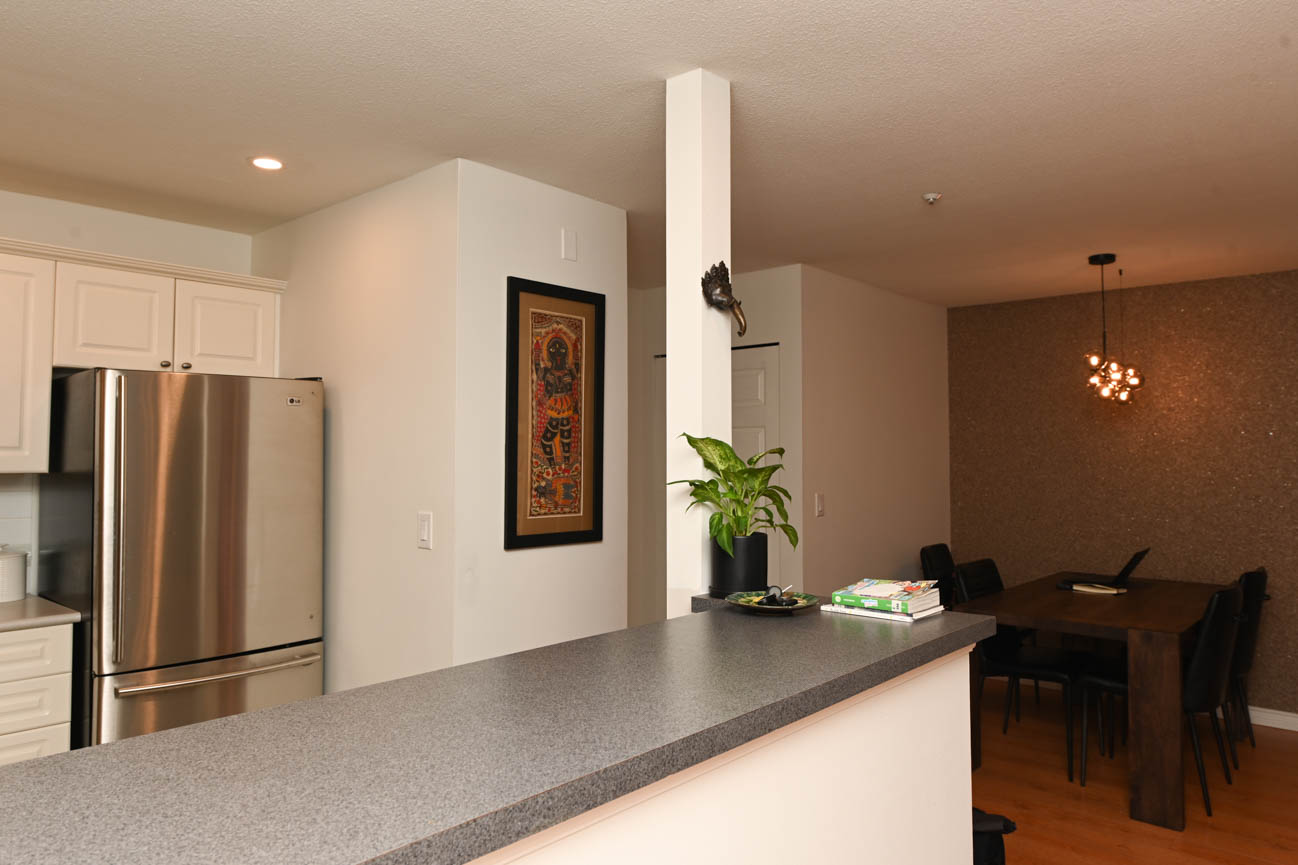 Bright kitchen with granite countertops and hardwood floors, featuring a stainless steel refrigerator and a potted plant.