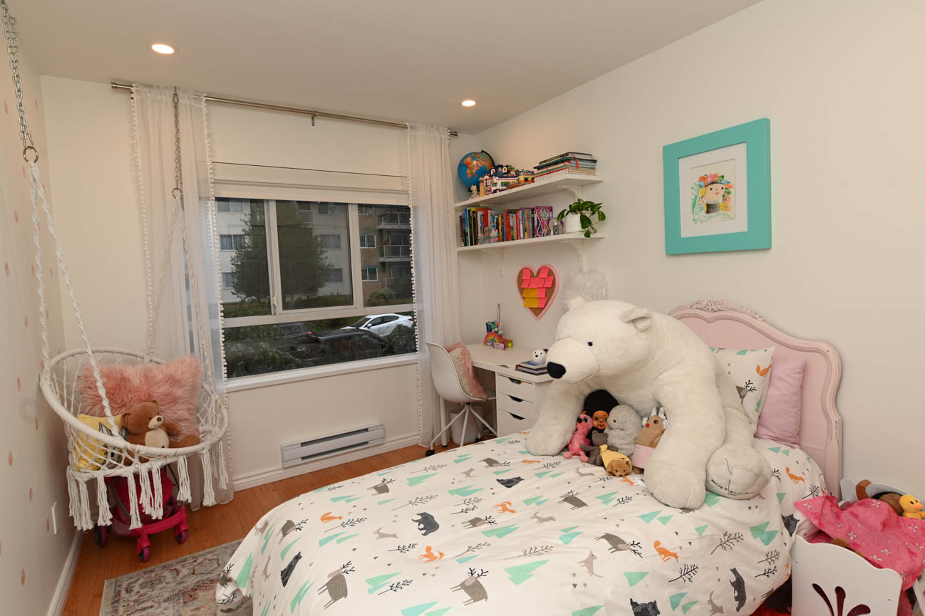 Bright bedroom with large window, plush toys, and a swing chair. - 208-128 8th Street West, North Vancouver