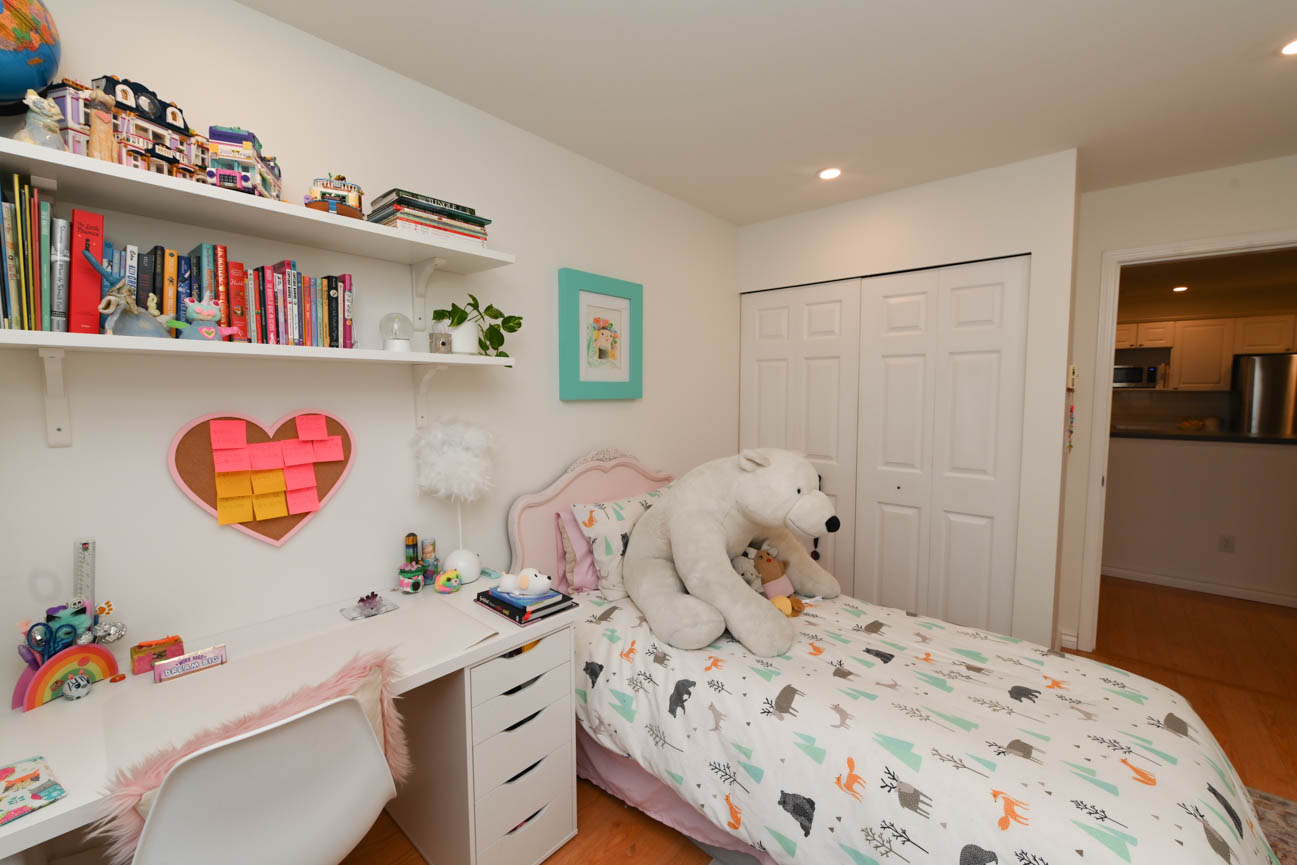 Bright bedroom with white furniture, colorful bedding, and bookshelves. - 208-128 8th Street West, North Vancouver