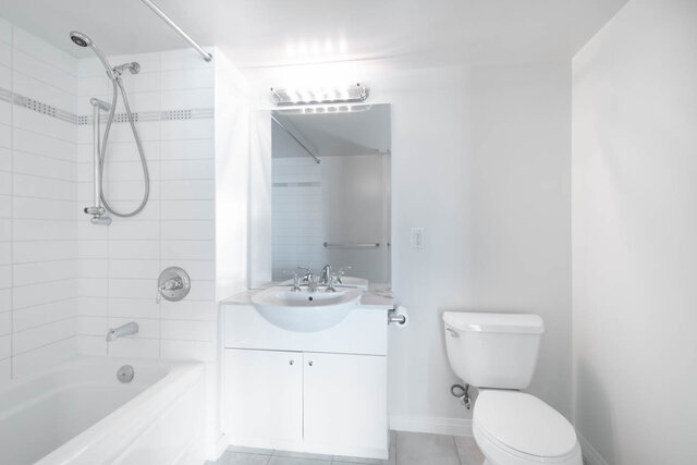 Bright bathroom with white fixtures, countertop, and large mirror. - 704-188 East Esplanade, North Vancouver