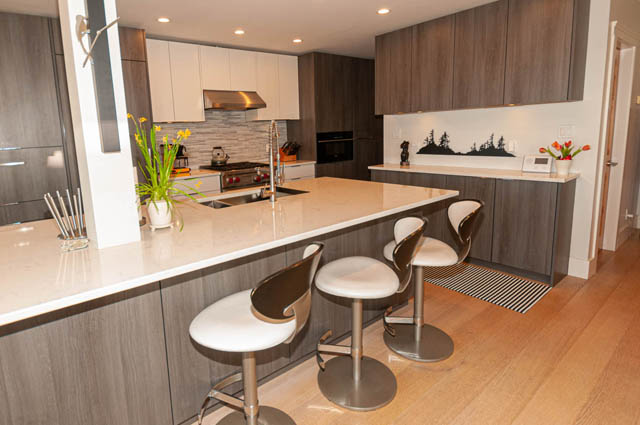 Modern kitchen with white countertops, hardwood floors, and a sleek island seating area. - 2128 Grand Blvd, North Vancouver