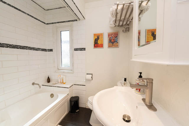 Bright bathroom with white subway tile walls and vintage posters on the wall. - 2128 Grand Blvd, North Vancouver