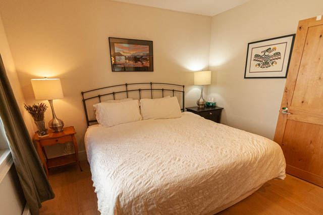 Spacious bedroom with a cozy bed, wooden floors, and framed artwork, perfect for a comfortable stay. - 2128 Grand Blvd, North Vancouver