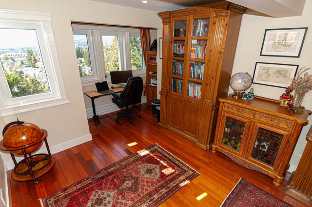 Spacious home office with hardwood floors, a large bookshelf, and a city view. - 2128 Grand Blvd, North Vancouver