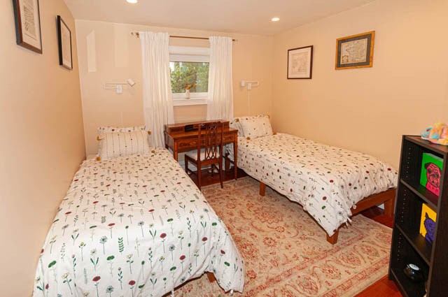 Spacious bedroom with twin beds, floral bedding, and a wooden desk by the window. - 2128 Grand Blvd, North Vancouver