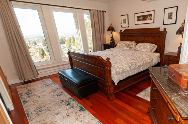 Spacious master bedroom with hardwood floors, large windows offering a city view, and a wooden bed frame. - 2128 Grand Blvd, North Vancouver