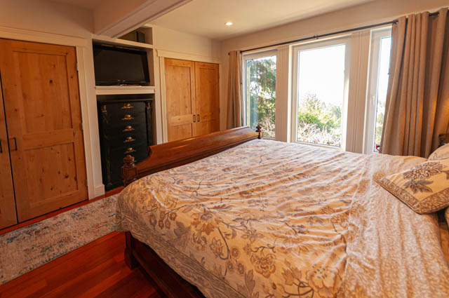 Spacious bedroom with wooden furniture, floral bedding, and large windows offering a view of greenery. - 2128 Grand Blvd, North Vancouver