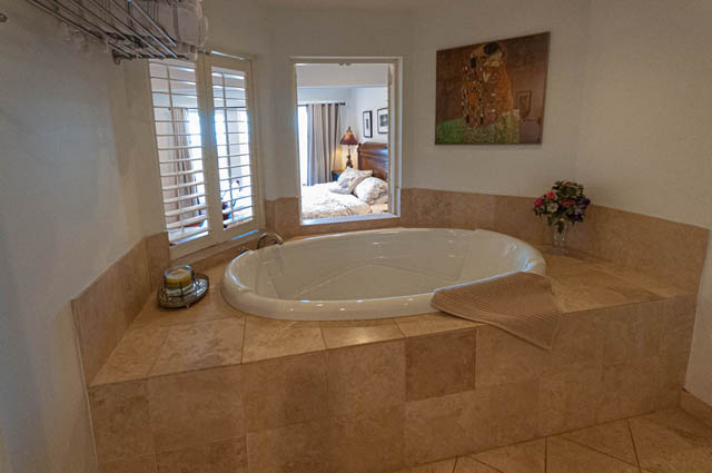Spacious master bathroom with a large soaking tub, beige tile, and a view of the bedroom. - 2128 Grand Blvd, North Vancouver