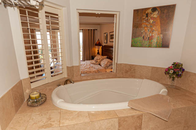Spacious master bathroom with a luxurious corner tub, beige tile counters, and a view into the bedroom. - 2128 Grand Blvd, North Vancouver