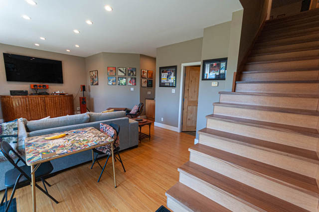 Spacious living room with hardwood floors, modern furniture, and a large TV above a wooden console. - 2128 Grand Blvd, North Vancouver