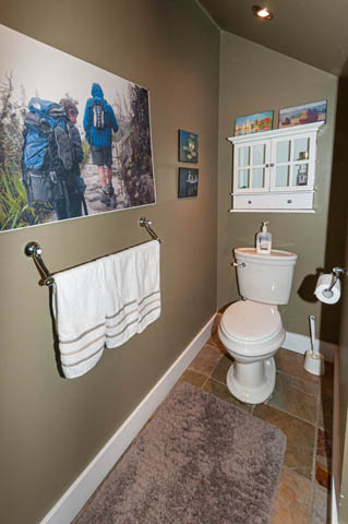Bathroom with stone flooring, wall art, and a cabinet above the toilet. - 2128 Grand Blvd, North Vancouver