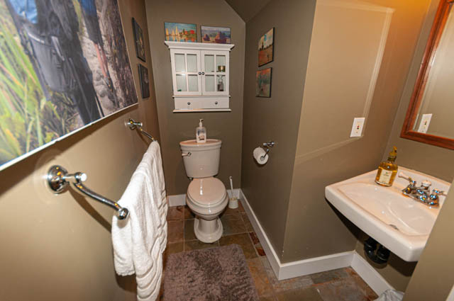 Bathroom with modern sink, toilet, and decorative wall art, featuring a cozy towel setup and a small cabinet for storage.