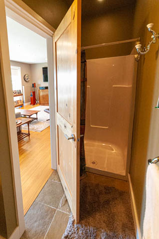 Bathroom with walk-in shower and wooden door, leading to hardwood flooring and living area. - 2128 Grand Blvd, North Vancouver