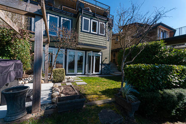 Spacious patio with stone accents and lush greenery, perfect for relaxation. - 2128 Grand Blvd, North Vancouver