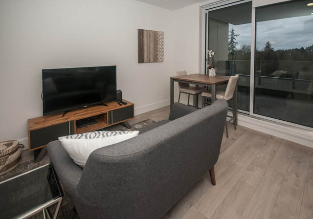 Bright living room with modern furniture, hardwood floors, and a city view. - 907 - 680 Seylynn Crescent, North Vancouver