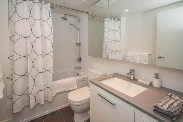 Furnished bathroom with modern sink, white countertop, and patterned shower curtain. - 907 - 680 Seylynn Crescent, North Vancouver