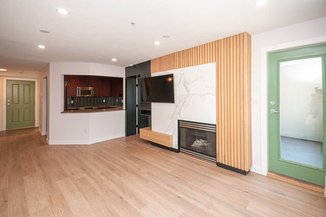 Open-concept living room with hardwood floors, modern fireplace, and kitchen counter in the background.