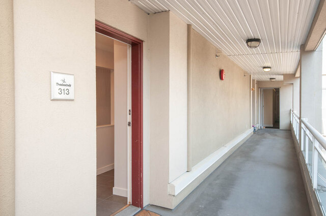 Spacious hallway leading to a cozy 2-bedroom condo, featuring a red door and beige walls. - 313 - 108 West Esplanade Ave, North Vancouver