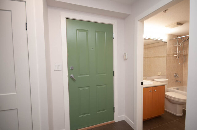 Modern bathroom with wooden cabinets and a green door. - 313 - 108 West Esplanade Ave, North Vancouver